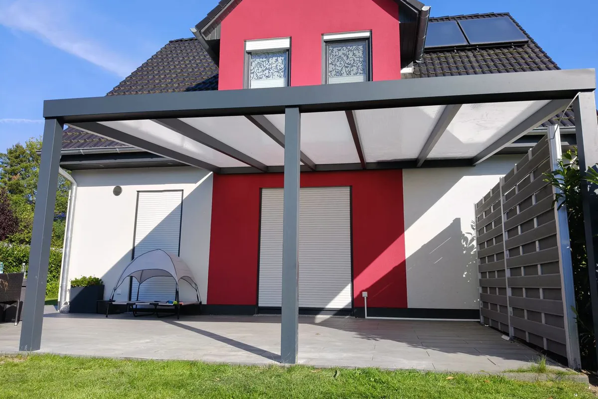 Terrassenüberdachung über die ganze Breite eines Hauses mit roter Fassade