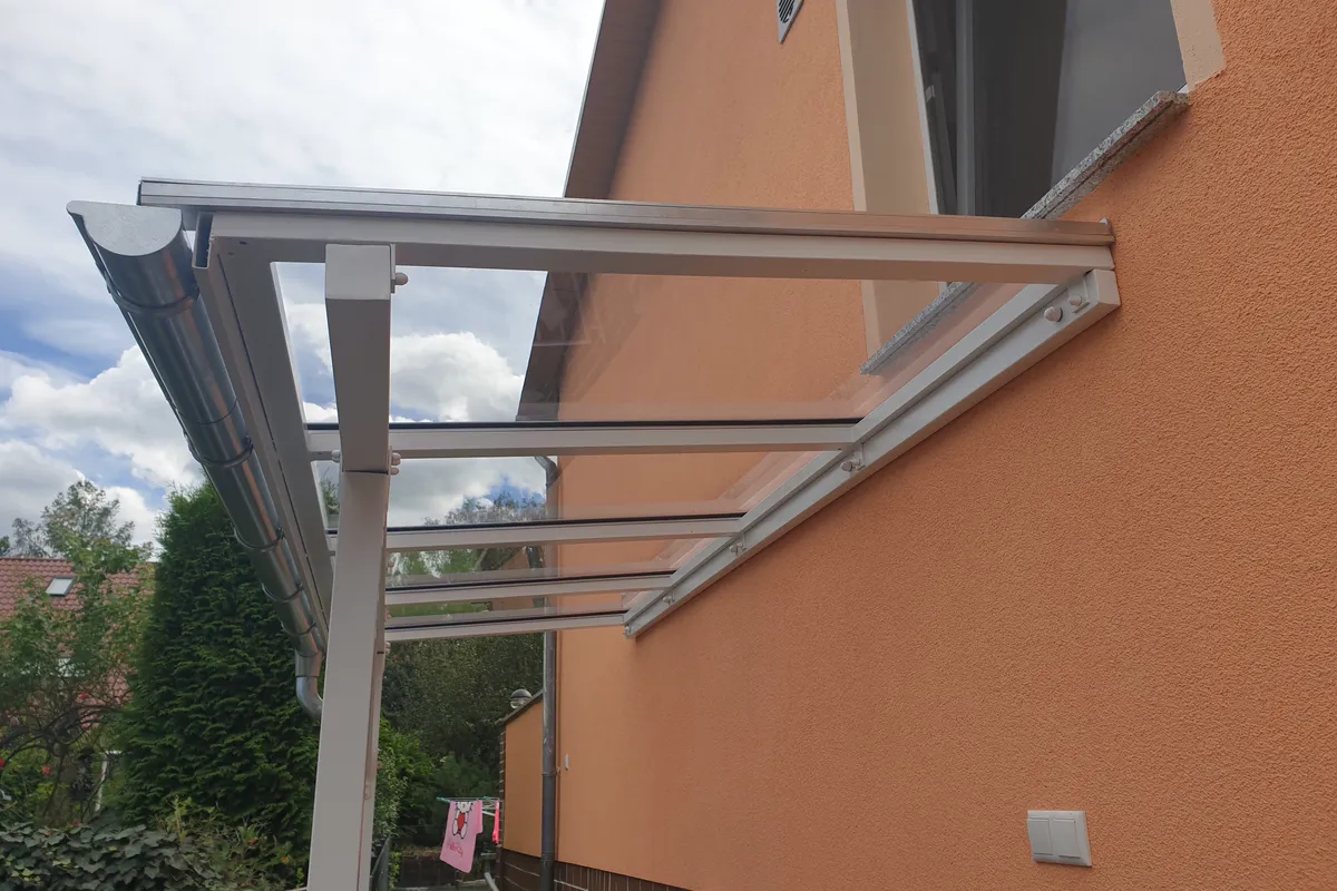 Vordach aus Aluminium mit Glasdach über einer Kellertreppe an einem Haus mit orangefarbener Fassade