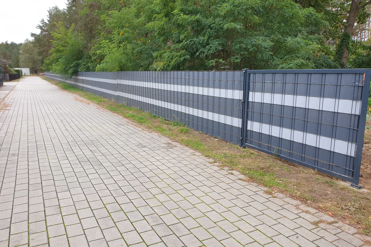 Doppelstabmattenzaun mit eingeflochtenen Sichtschutzstreifen in Anthrazit und Hellgrau entlang eines Gehwegs