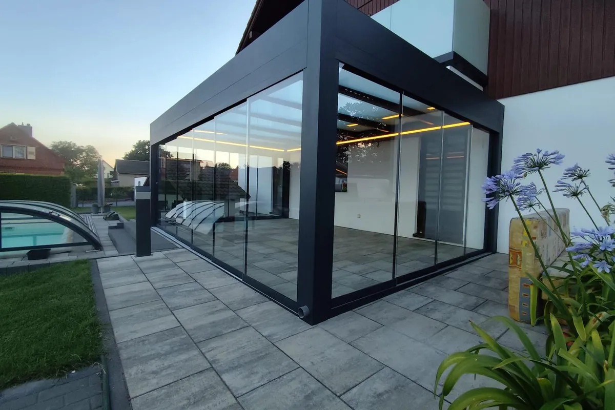 Anthrazitfarbene, rundum verglaste Pergola mit LED-Lichtleisten neben einem Pool