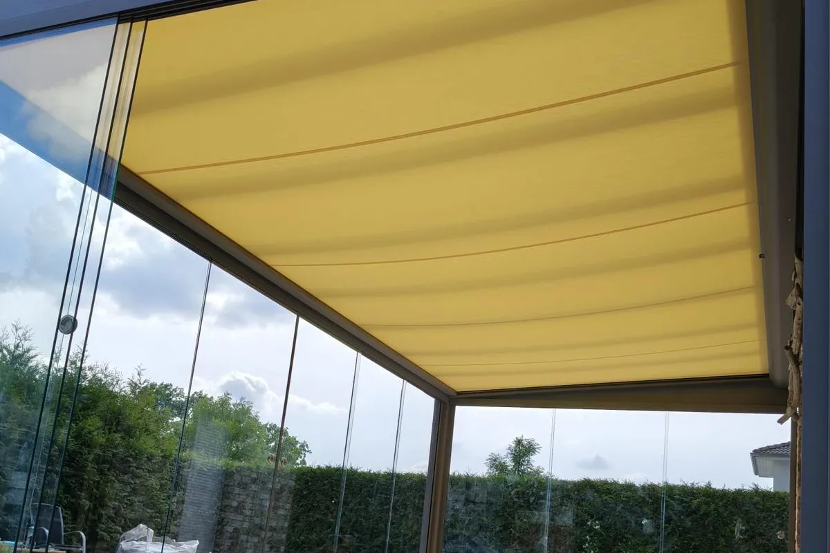 Pergola mit gelbem Stoffdach und Glasschiebewänden, Blick von innen in den Garten
