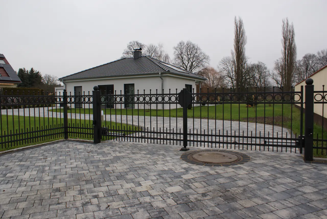 Geschweißter schwarzer Stahlzaun mit Ringornament, Kugelkappen und Einfahrtstor vor einem Bungalow