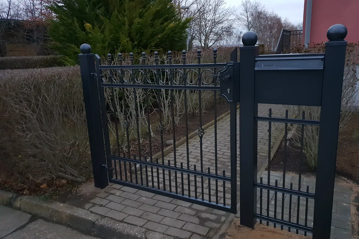 Stahlpforte mit Kugelkappen auf den Pfosten neben einem Zaunfeld
