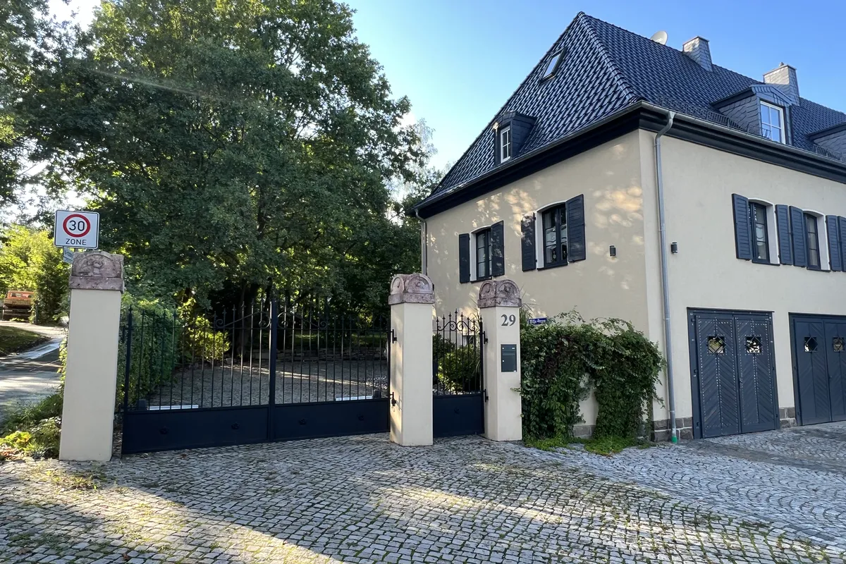 Zweiflügeliges Stahltor zwischen hellen Pfeilern vor einer Stadtvilla