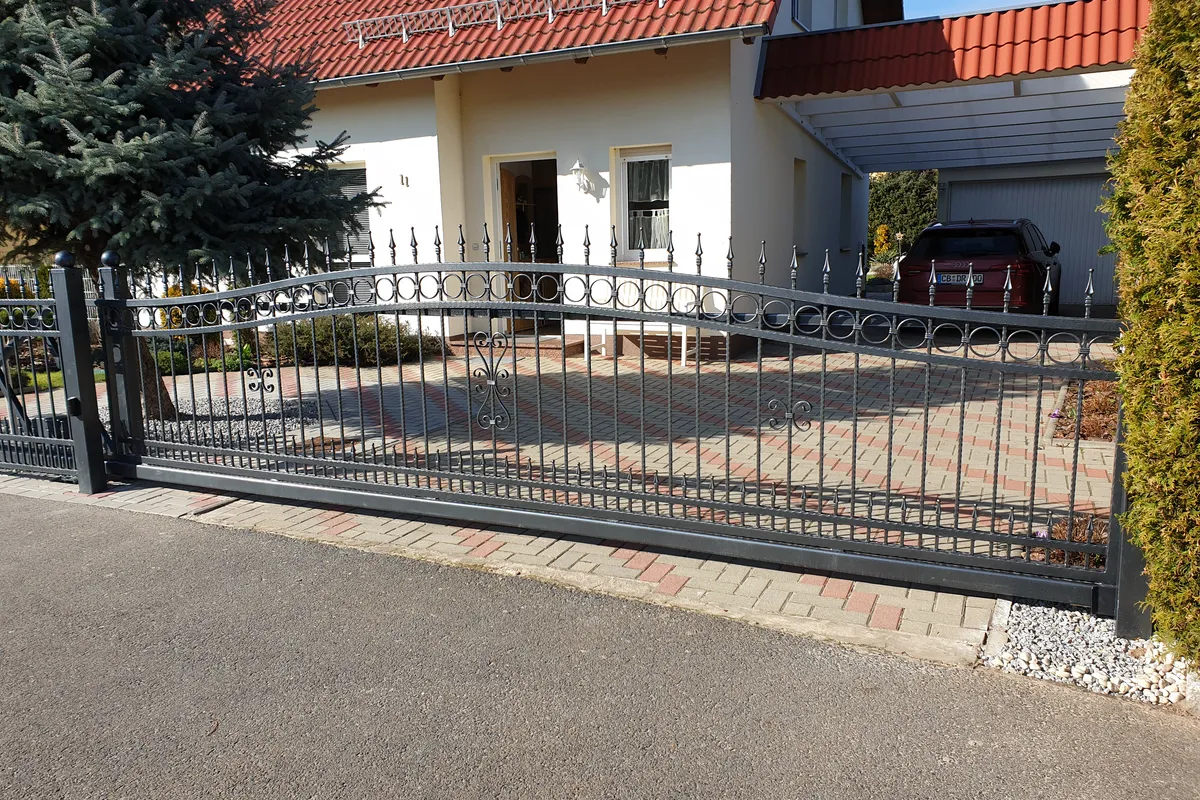 Geschweißtes Stahl-Schiebetor mit Bogen und Spitzen vor einem Einfamilienhaus mit Carport